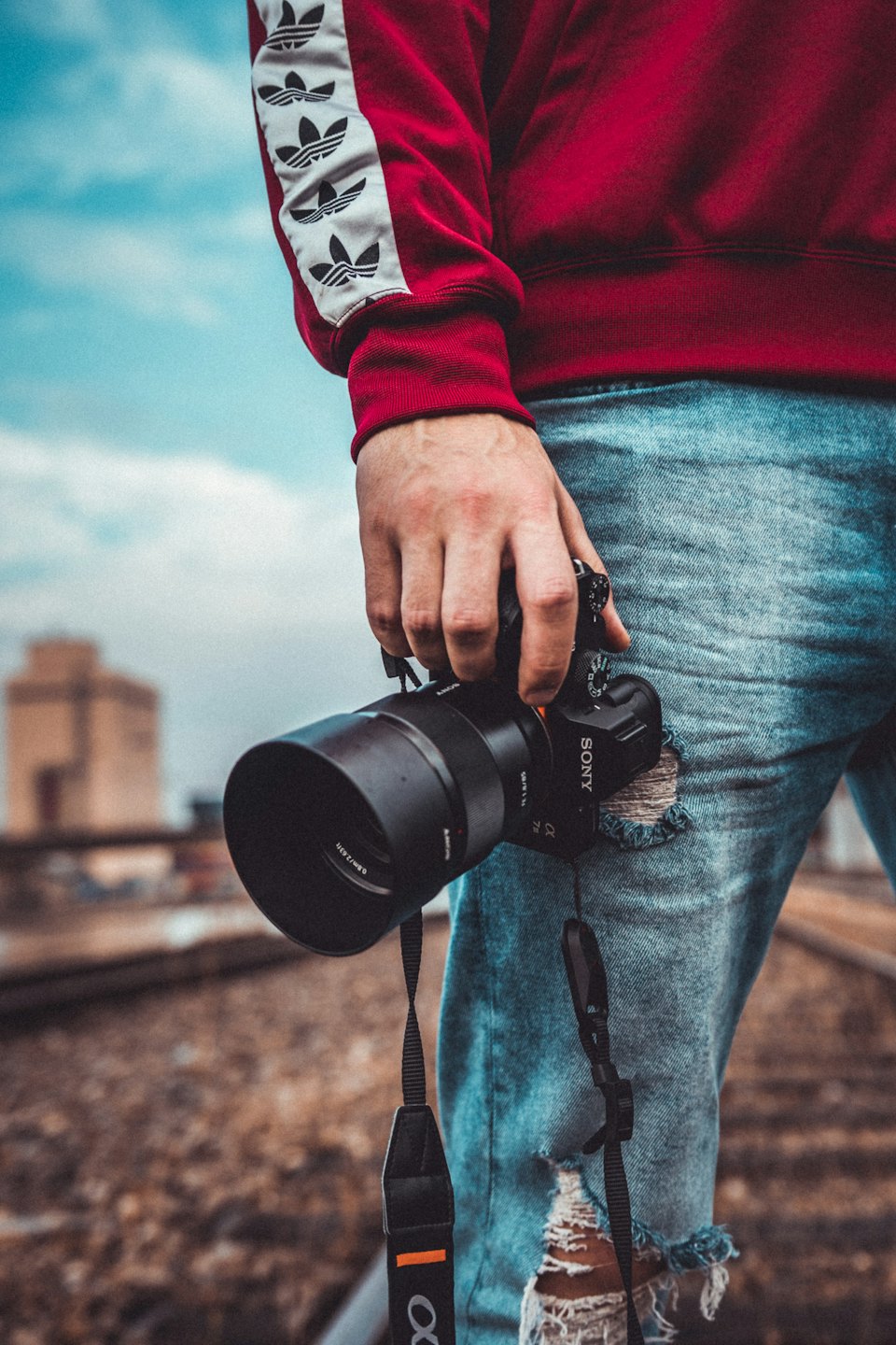 En fotograf i en röd sweatshirt håller en professionell kamera på ett järnvägsspår.