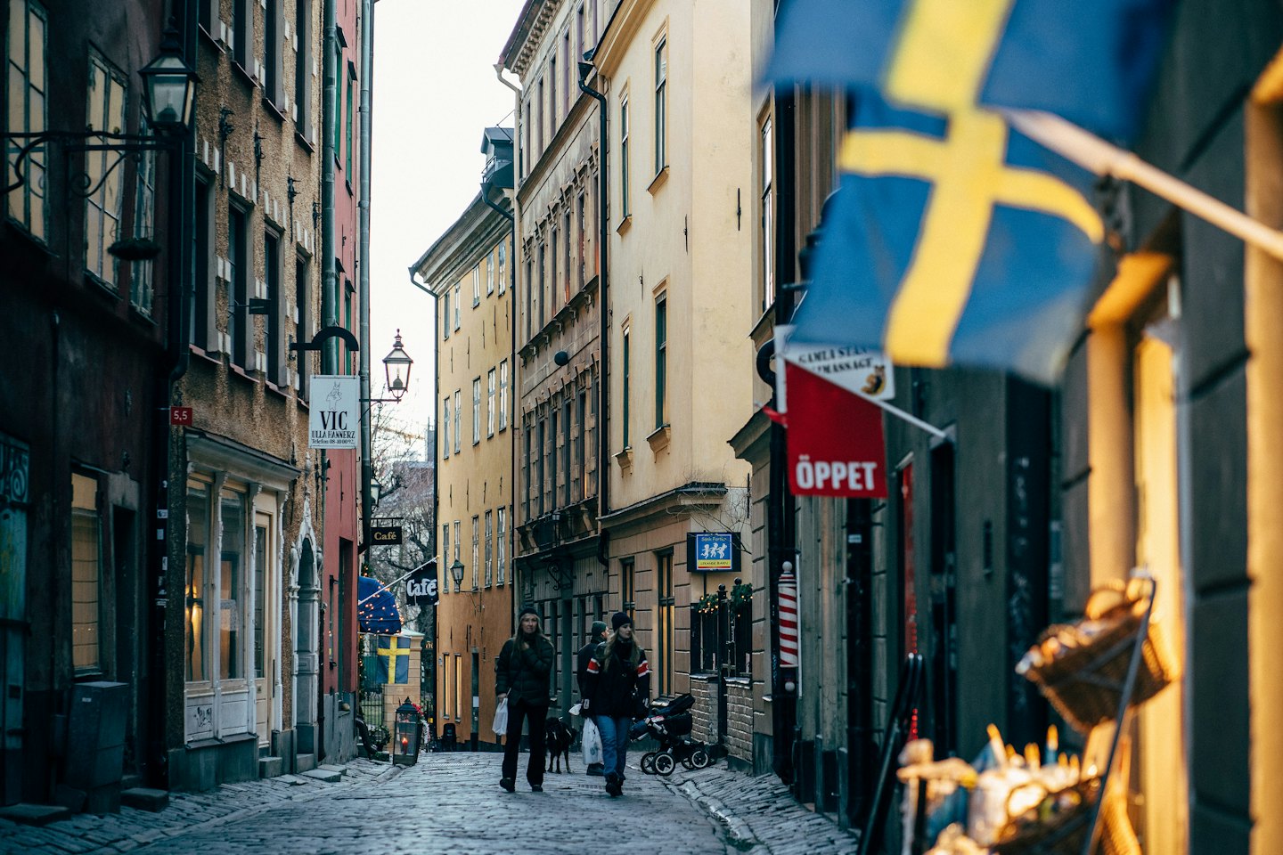 Två personer puttar en barnvagn nerför en smal kullerstensgata.