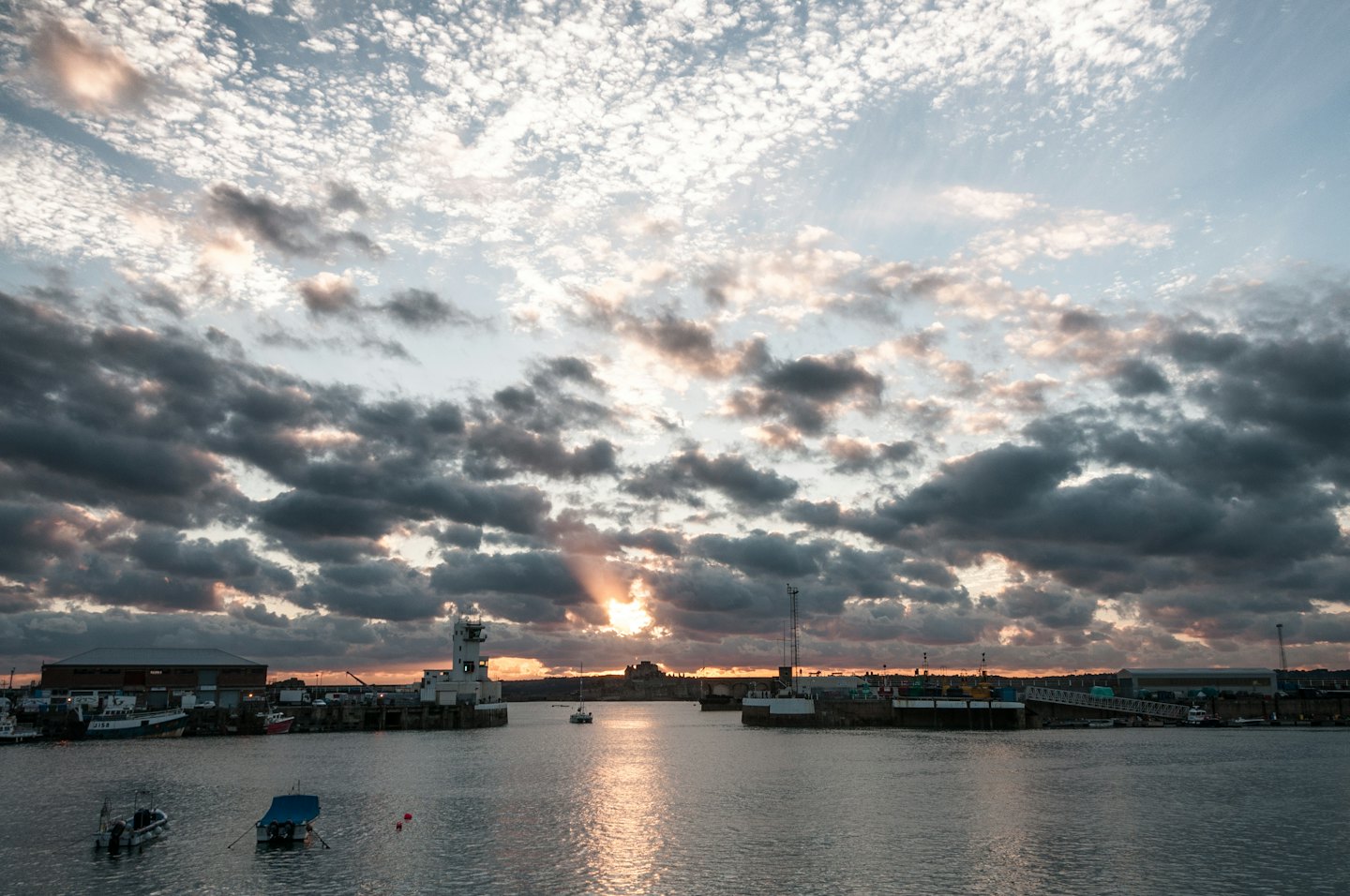 Små båtar ligger förtöjda i en lugn hamn med industribyggnader.