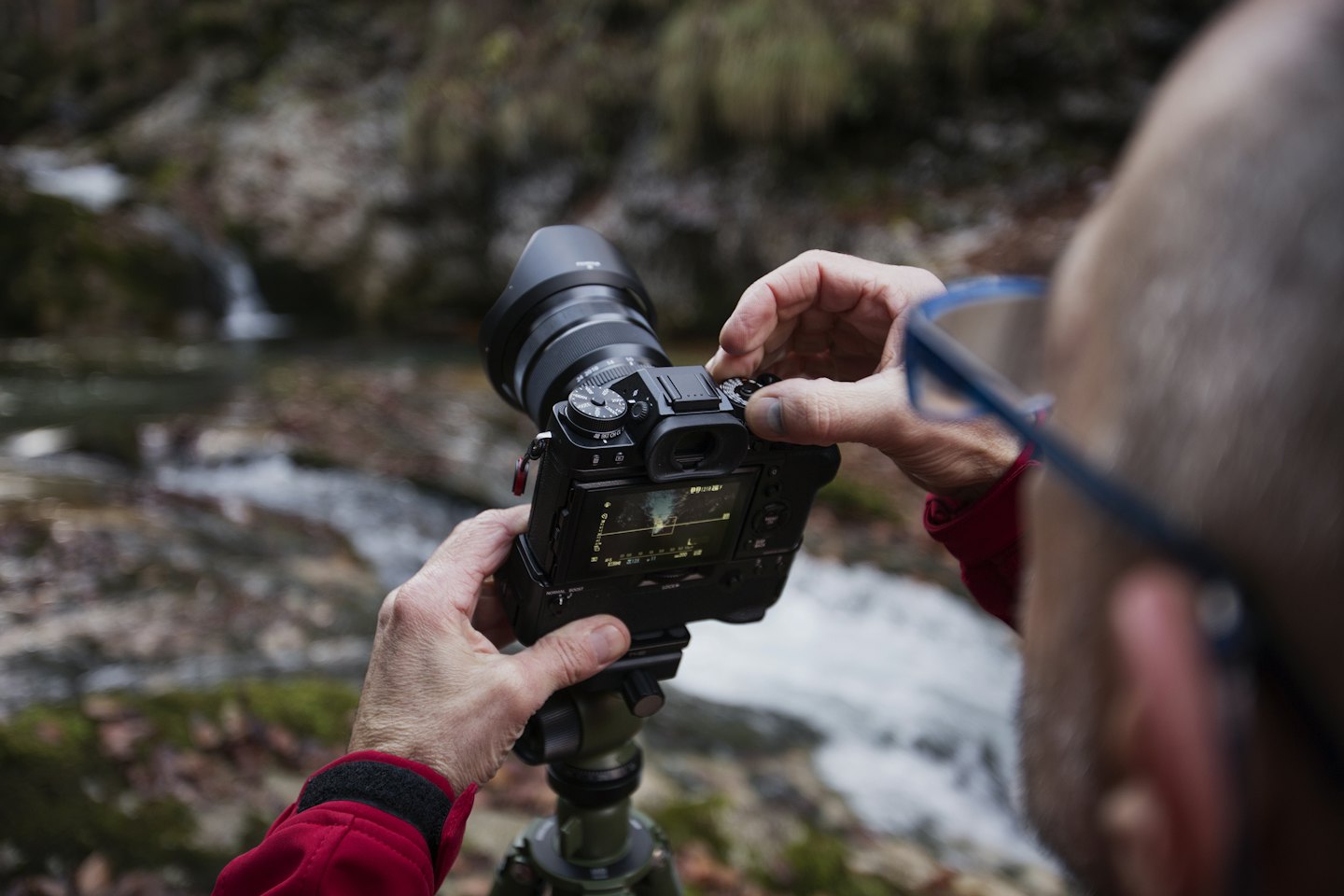 Fotograf i röd jacka justerar spegellös kamera på stativ.